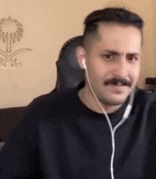 a man with a mustache is sitting in a chair wearing headphones and making a funny face .