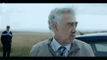 a man with gray hair and a mustache is standing in front of a police car