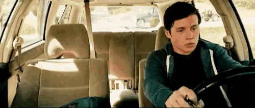 a young man is sitting in the driver 's seat of a car and holding a key .