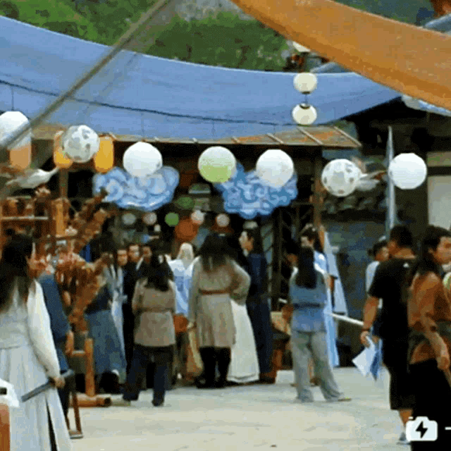 a group of people are gathered in front of a building with balloons hanging from the roof