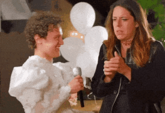 a man in a white dress is holding a microphone while a woman looks on