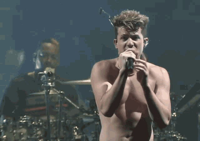 a shirtless man is singing into a microphone on stage