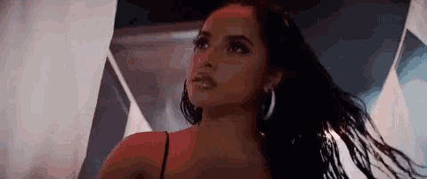 a woman in a black top and hoop earrings is standing in front of a white curtain .