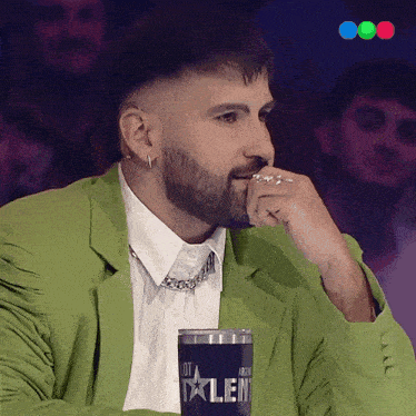 a man in a green jacket sits in front of a blue cup that says talent