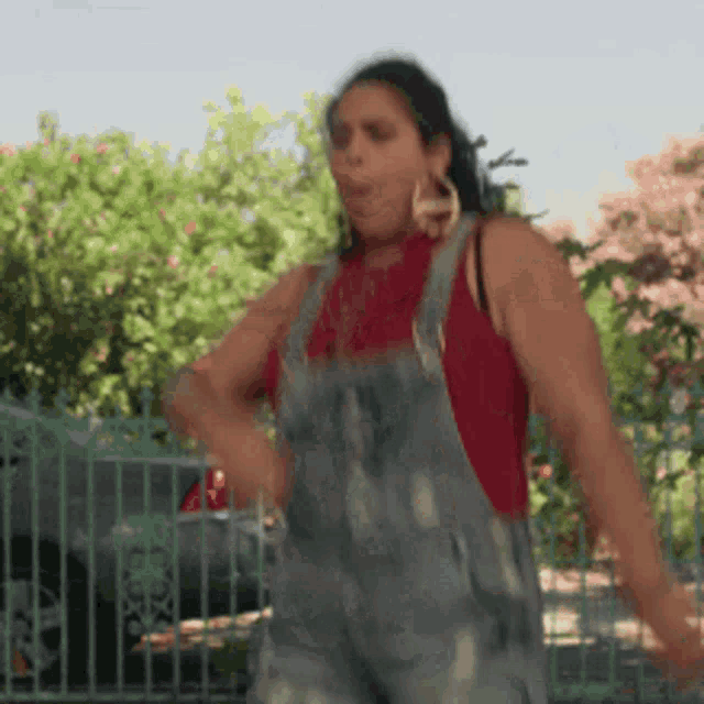 a woman in overalls is dancing in front of a green fence