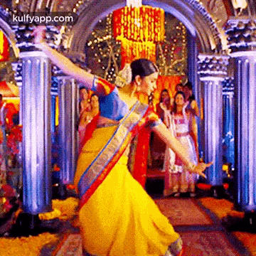 a woman in a yellow saree is dancing in front of a crowd of people .