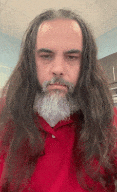 a man with long hair and a beard is wearing a red polo shirt