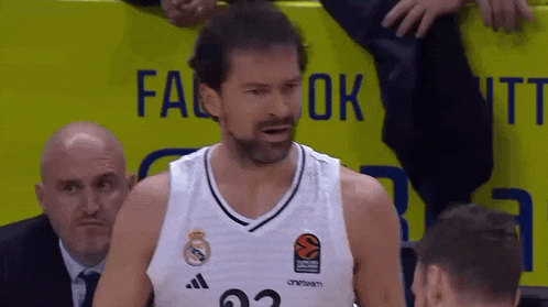 a basketball player with a beard is standing in front of a yellow sign that says ok .