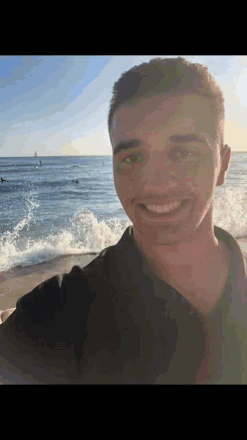 a young man taking a selfie on the beach with the ocean in the background
