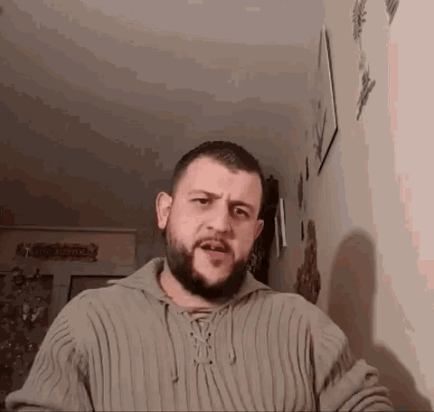a man with a beard wearing a sweater is standing in front of a wall with a sign that says welcome