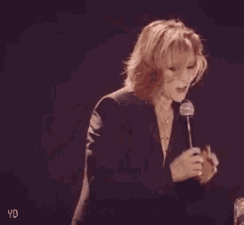 a woman in a suit is holding a microphone in her hand .