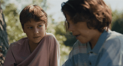 two young boys are sitting under a tree and talking