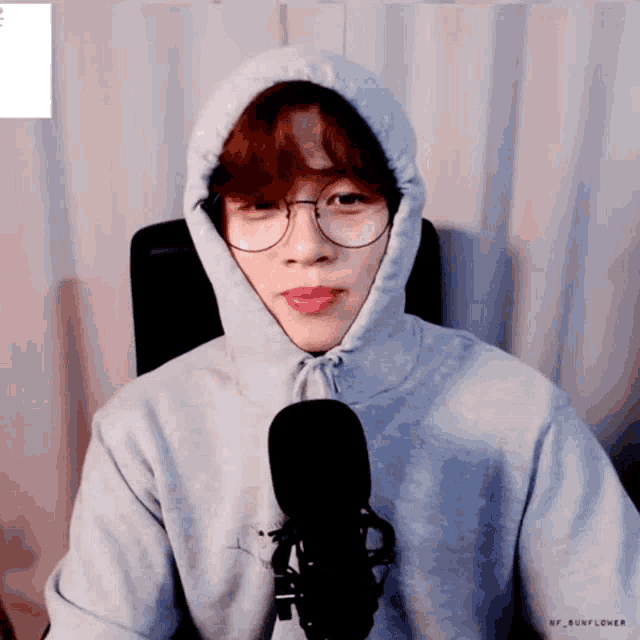 a person wearing a hoodie and glasses sitting in front of a microphone