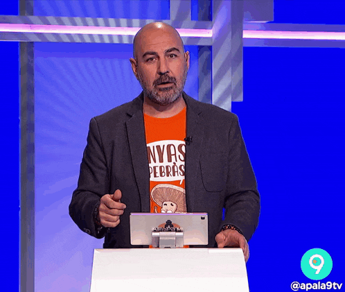 a man wearing a nyas pebras shirt is standing in front of a podium