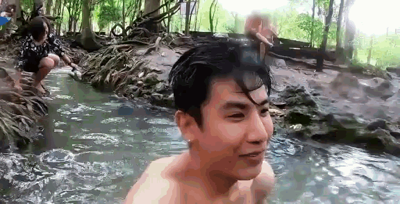 a man without a shirt is standing in a stream of water .