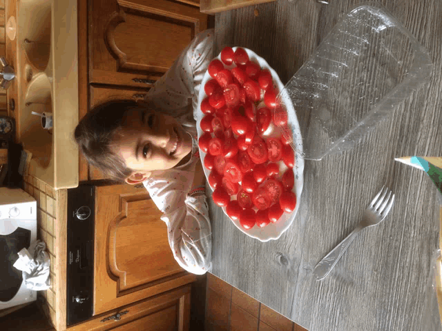 a little girl is sitting at a table with a plate of tomatoes on it