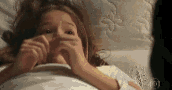a young girl is laying in bed with her hands on her face .