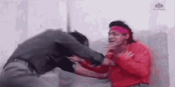 two men are fighting each other in a room with a wall in the background .