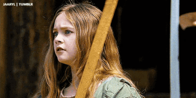 a young girl with long red hair is holding a wooden stick in her right hand ..