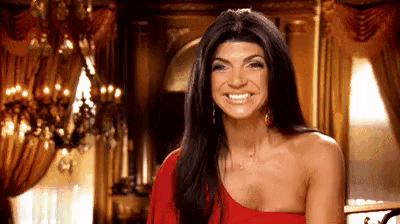 a woman in a red dress is smiling in front of a chandelier in a room .