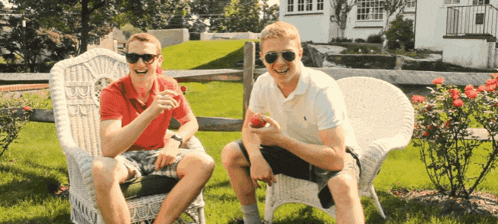 two men are sitting in wicker chairs and one of them is eating a strawberry