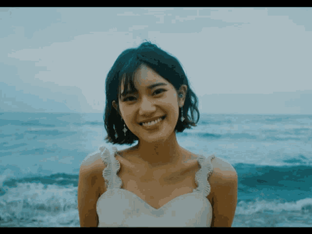 a woman in a white dress smiles while standing on the beach