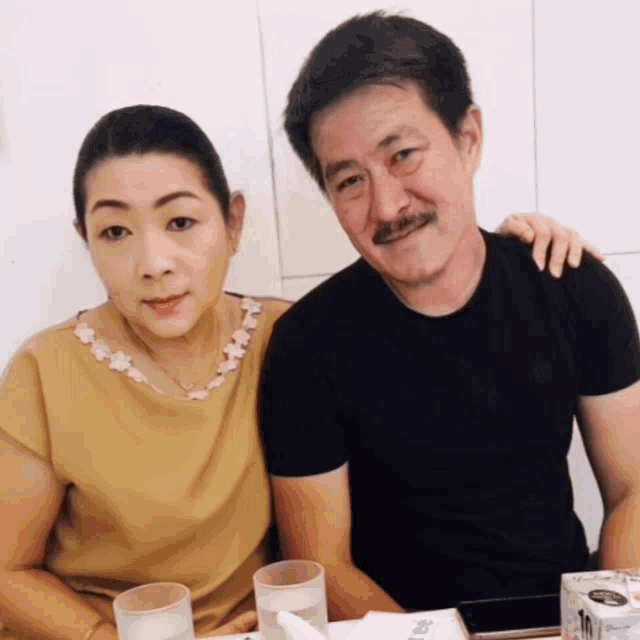 a man and a woman sit at a table with a box of tissues