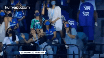 a group of people wearing masks are sitting in a stadium watching a cricket game .