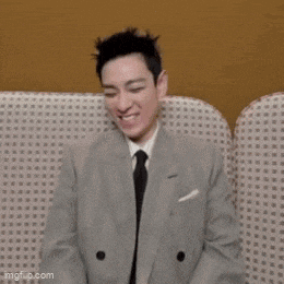 a man in a suit and tie is sitting on a couch smiling