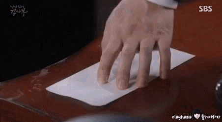 a man 's hand is holding a piece of paper on a table .