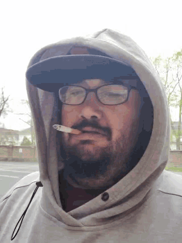a man wearing glasses and a hooded sweatshirt smoking a cigarette