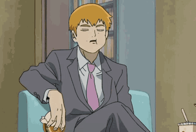a man in a suit and tie is sitting on a couch and eating a hamburger