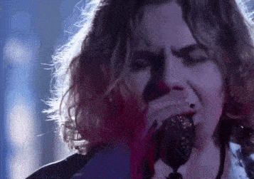 a man with curly hair is singing into a microphone .