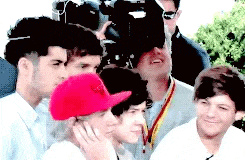 a group of young men are posing for a picture in front of a camera . one of the men is wearing a red hat .