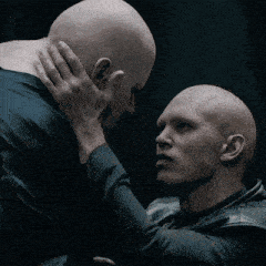two bald men looking at each other with one holding the other 's neck