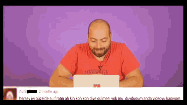 a bald man in a red shirt is sitting in front of a laptop computer