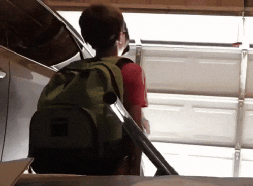 a boy with a green backpack stands in a garage
