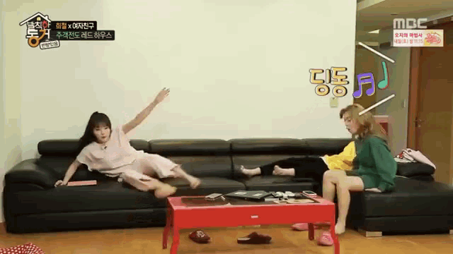 two girls are sitting on a couch in front of a sign that says mbc on it
