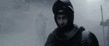 a man wearing a helmet and chain mail stands in a foggy forest