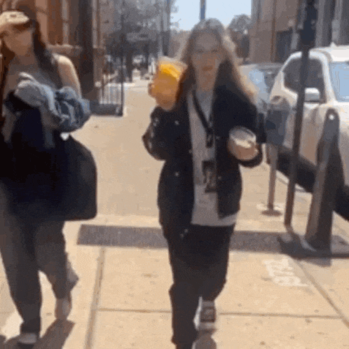 two women are walking down a sidewalk on a sunny day .