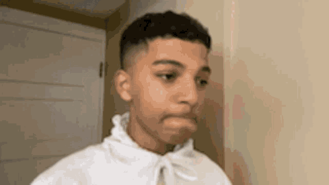 a young man in a white hoodie is making a funny face while standing in front of a door .
