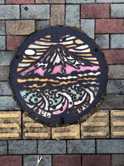 a manhole cover on a brick sidewalk has a picture of a mountain and waves on it