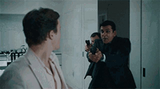 a man in a suit pointing a gun at another man in a pink shirt