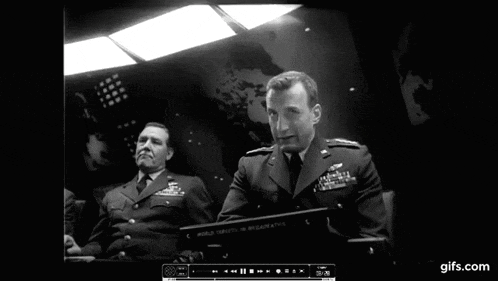 two men in military uniforms are sitting in front of a computer screen that says world defense