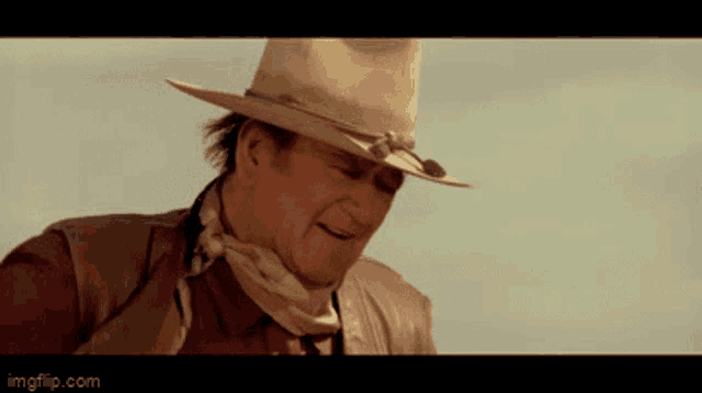 a man wearing a cowboy hat and a scarf around his neck is standing in the desert