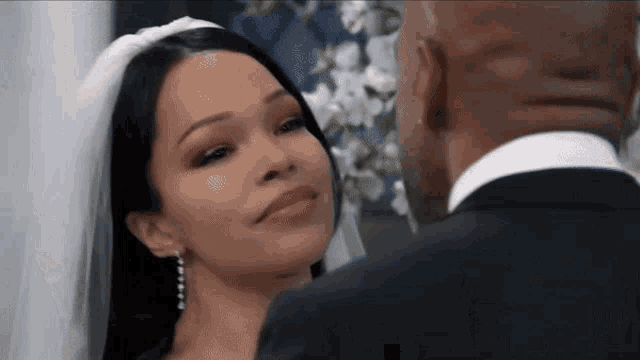 a bride and groom are looking at each other during their wedding ceremony and the bride is smiling .