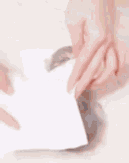 a person is holding a pen over a kitten wrapped in a piece of paper .
