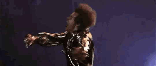 a man in a leather jacket is dancing on a stage in front of a blue background .