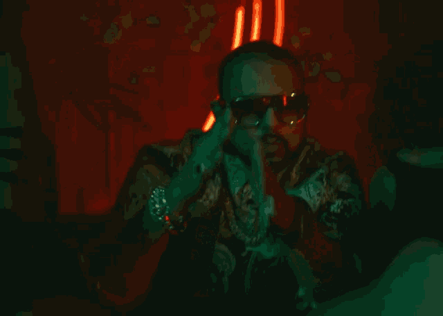 a man wearing sunglasses is sitting in front of a neon light