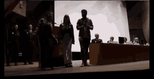 a group of people are standing on a stage with a man holding a microphone in front of them